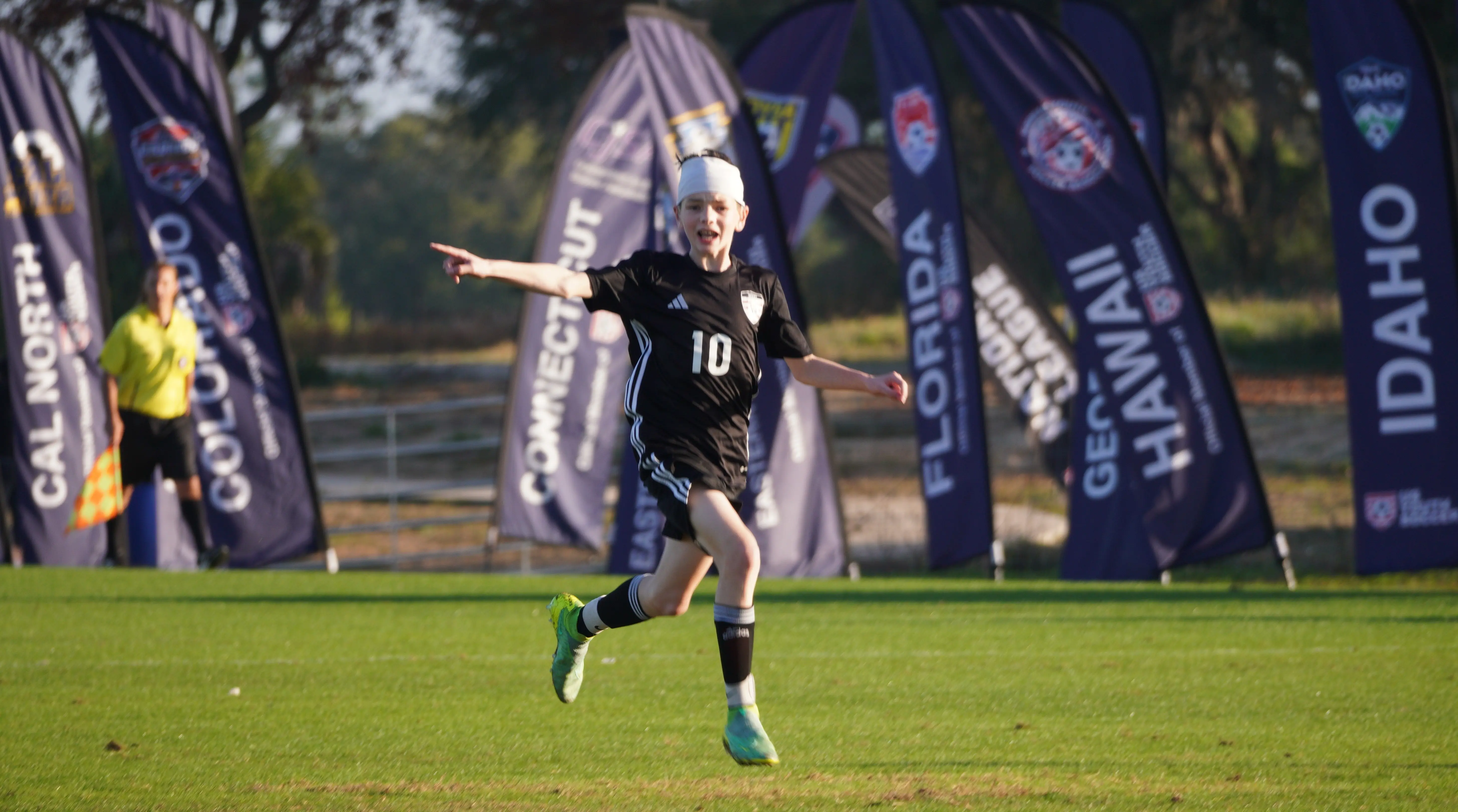 Daylen Hammon #10 in black ODP kit celebrating goal with arms out at ODP Regionals Orlando FL January 2024 with state banners in background